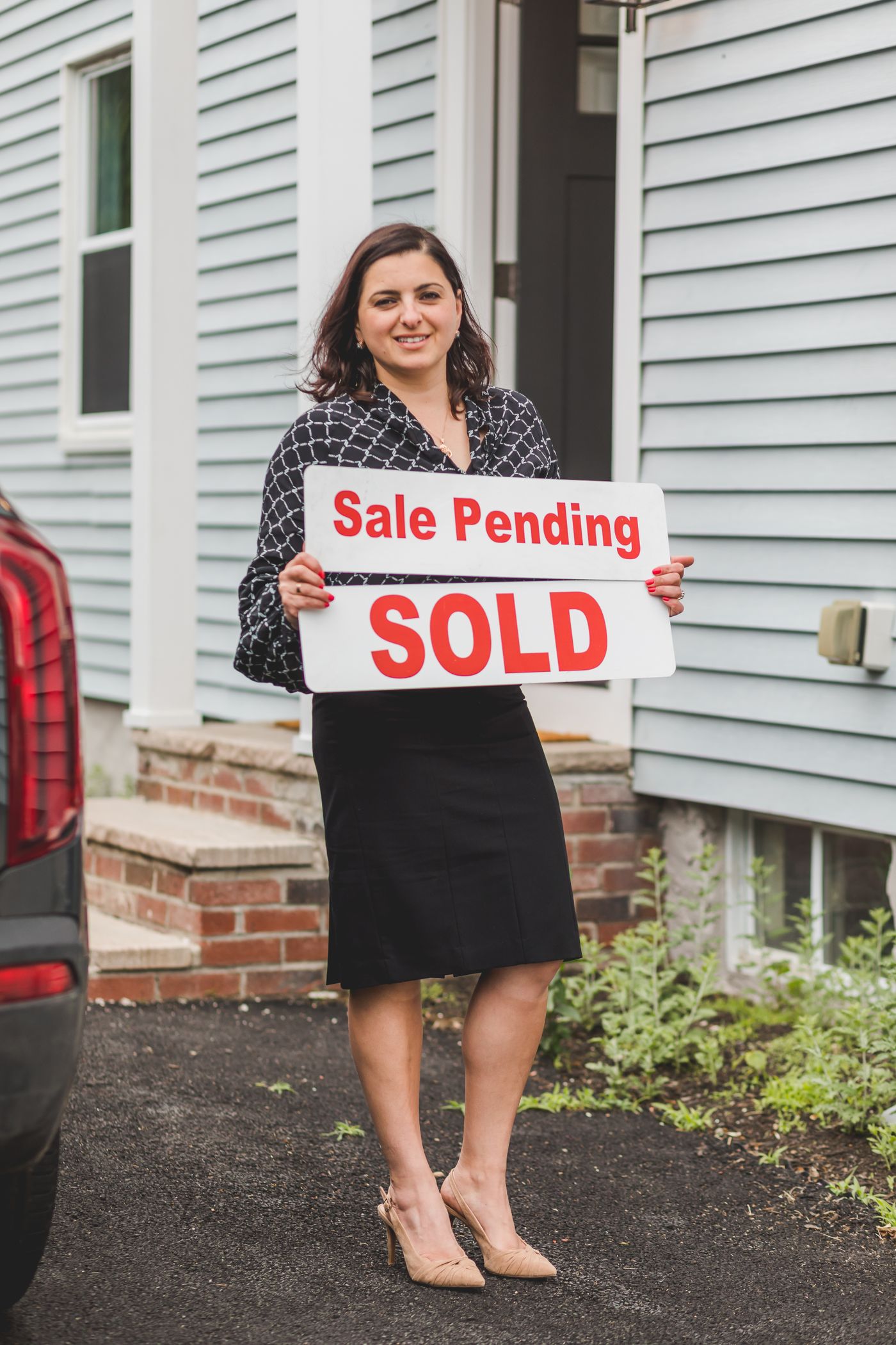 A real estate professional holding a sold sign outside a home